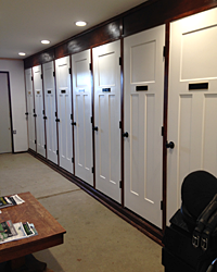 A row of clean, white, enclosed storage lockers or tack room cabinets with dark wood trim.