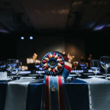 A close-up of a decorative red, gold, and blue equestrian ribbon placed on a formal dinner table.