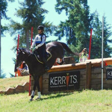 Eventing horse and rider jumping over a large log obstacle on a cross country course sponsored by Kerrits.